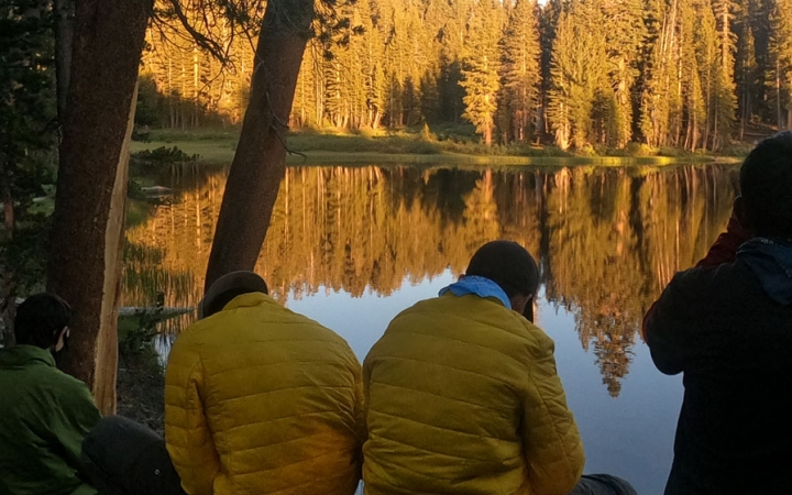 a group of people rest beside a body of water reflecting the trees
